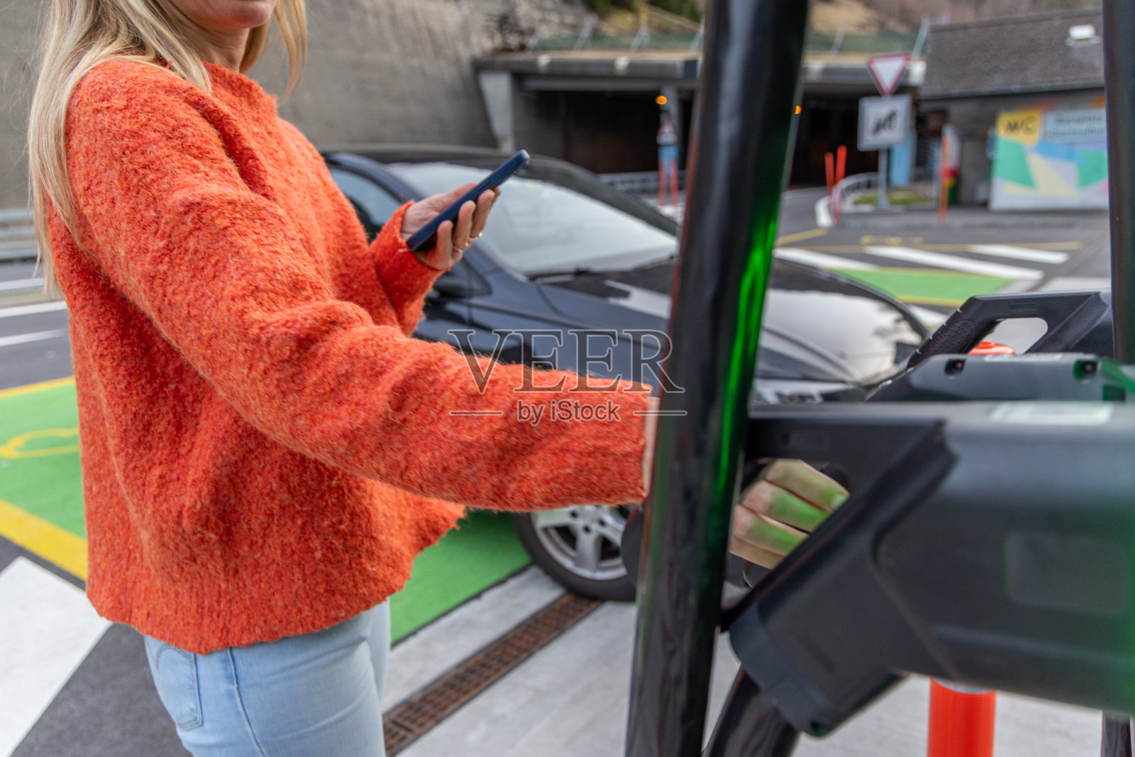 一名携带手机的女性在公共充电站设置了一款为电动汽车充电的移动应用程序照片摄影图片