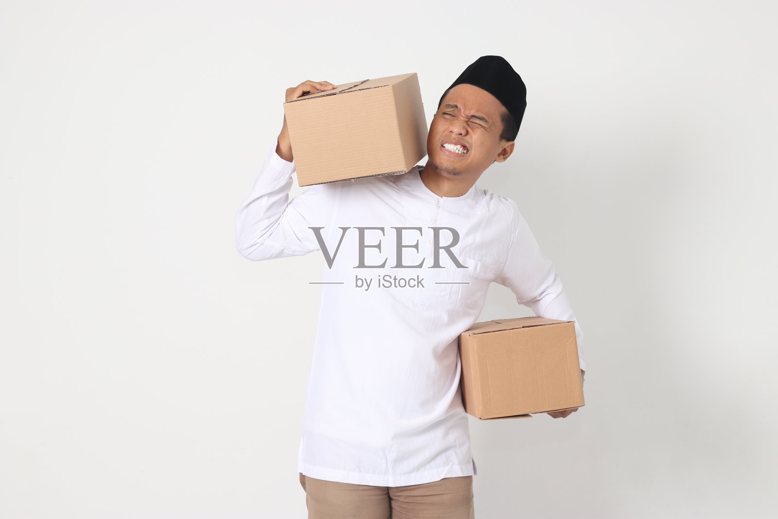 疲惫的亚洲穆斯林男子的肖像，穿着科科衬衫，带着peci，难以搬运纸板。回家过开斋节。白色背景上的孤立图像照片摄影图片