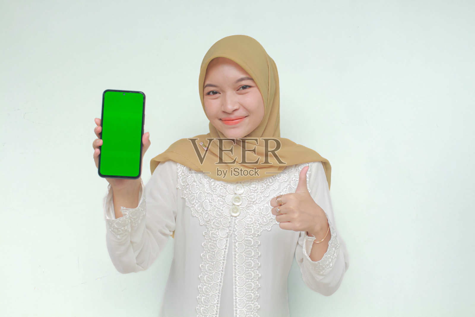 微笑的年轻亚洲穆斯林妇女展示手机绿屏推荐应用程序照片摄影图片