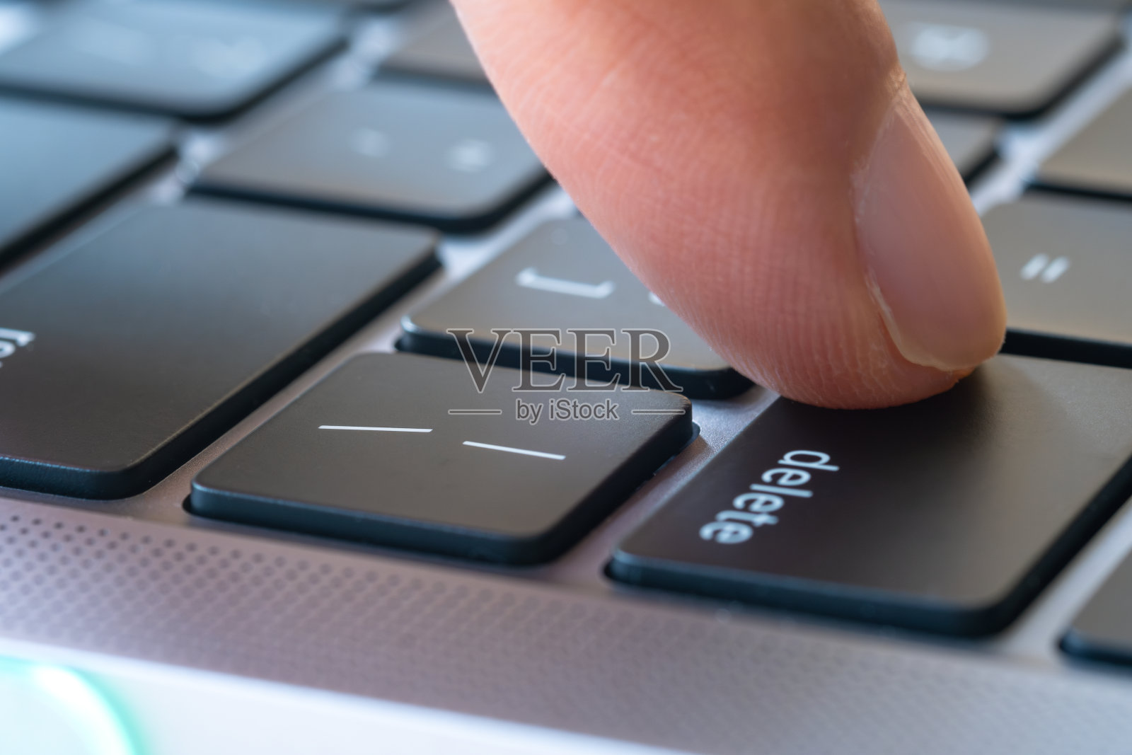 电脑用户的手指，他按下了电脑键盘上的删除键。照片摄影图片