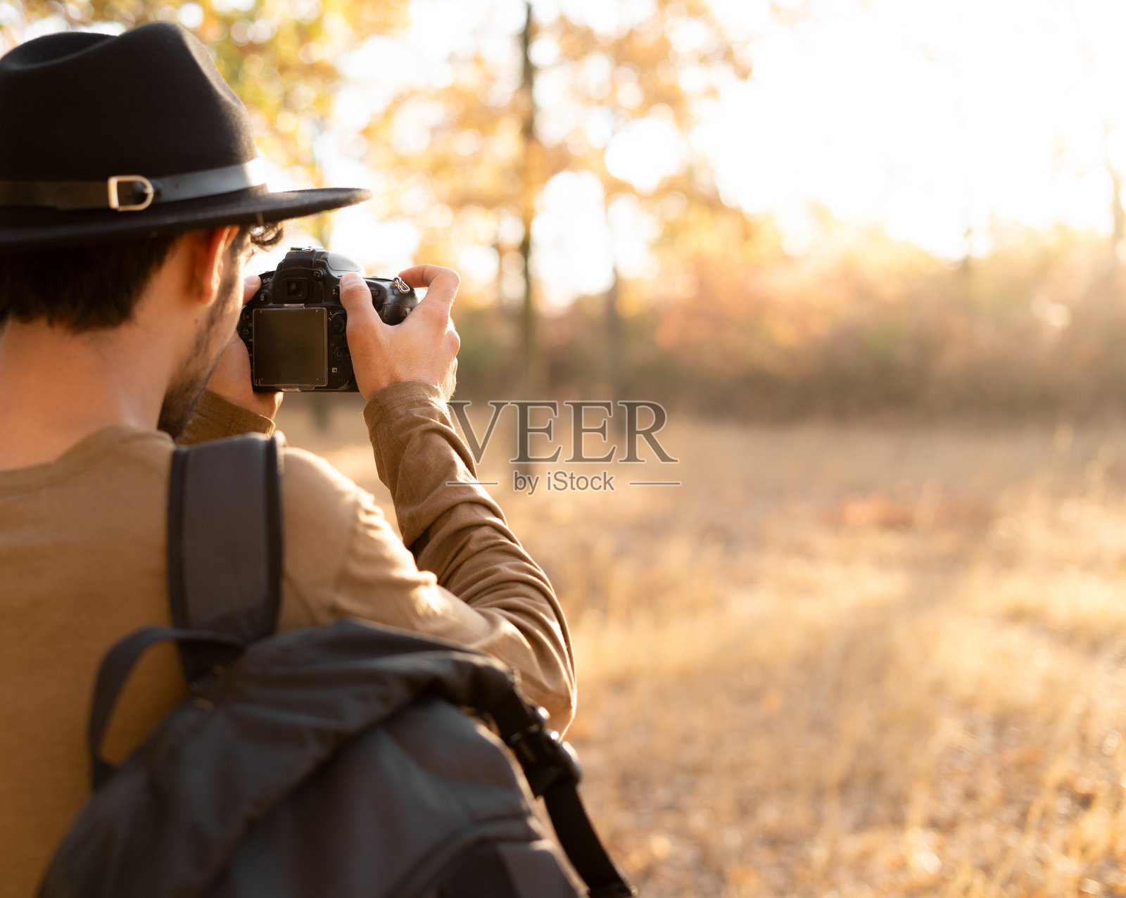 拍摄大自然的男游客。戴帽子的男人背着单反相机在秋天的森林里徒步旅行。照片摄影图片