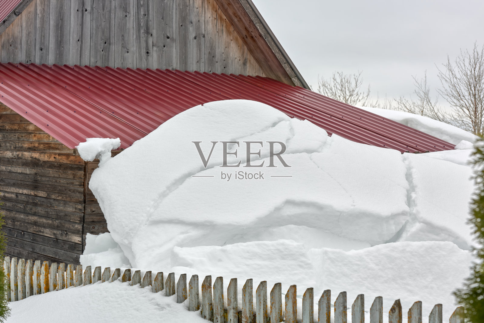 一大片雪堆从屋顶上滑落下来。春天解冻。照片摄影图片