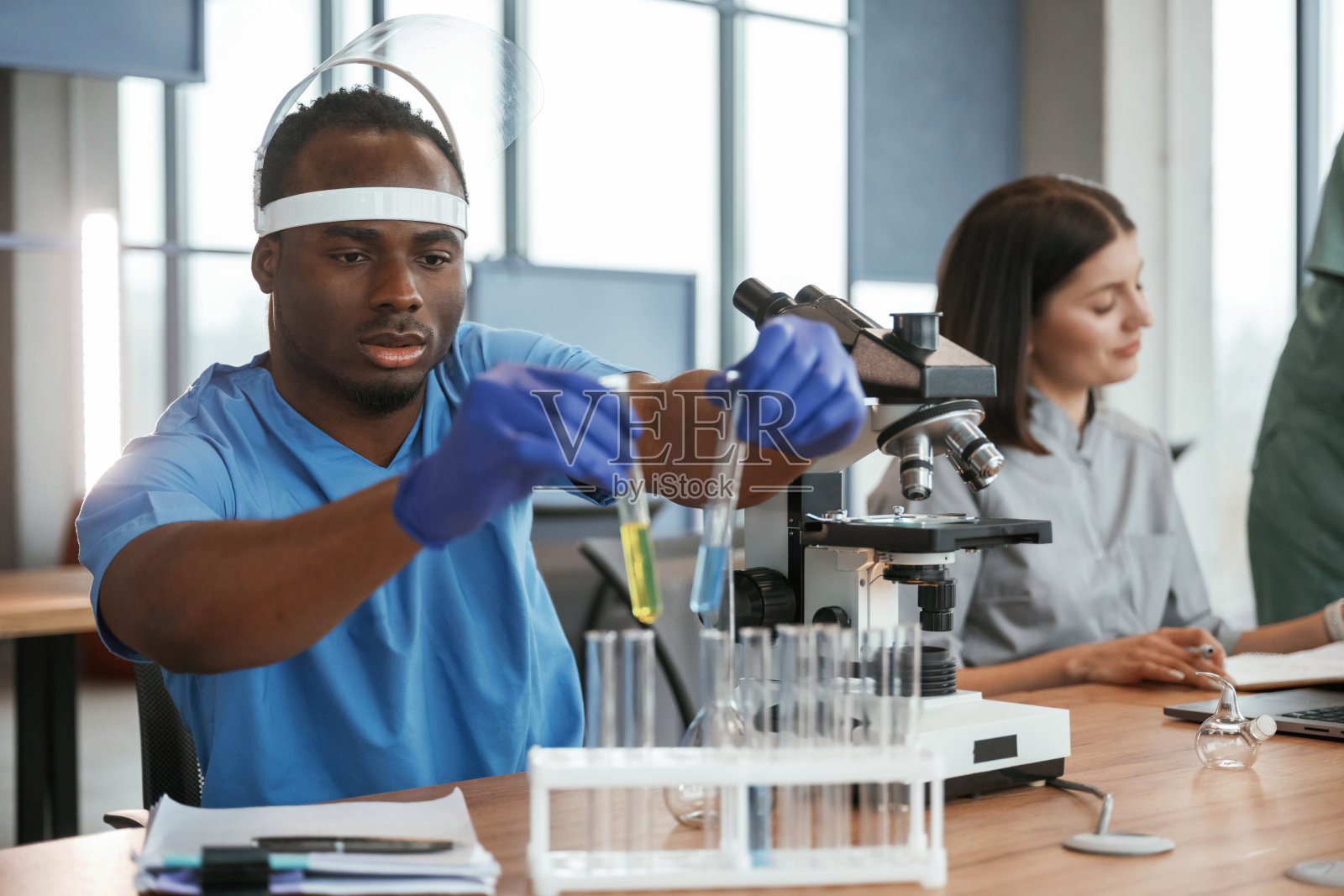 在实验室里用试管和显微镜工作。一群医生聚集在室内照片摄影图片