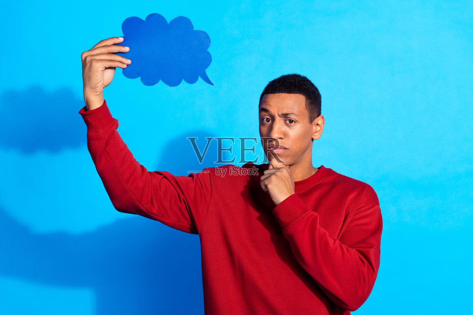 聪明沉思的男人的肖像，手摸下巴，拿着空白的空间，泡泡卡片，在蓝色的背景上沉思照片摄影图片