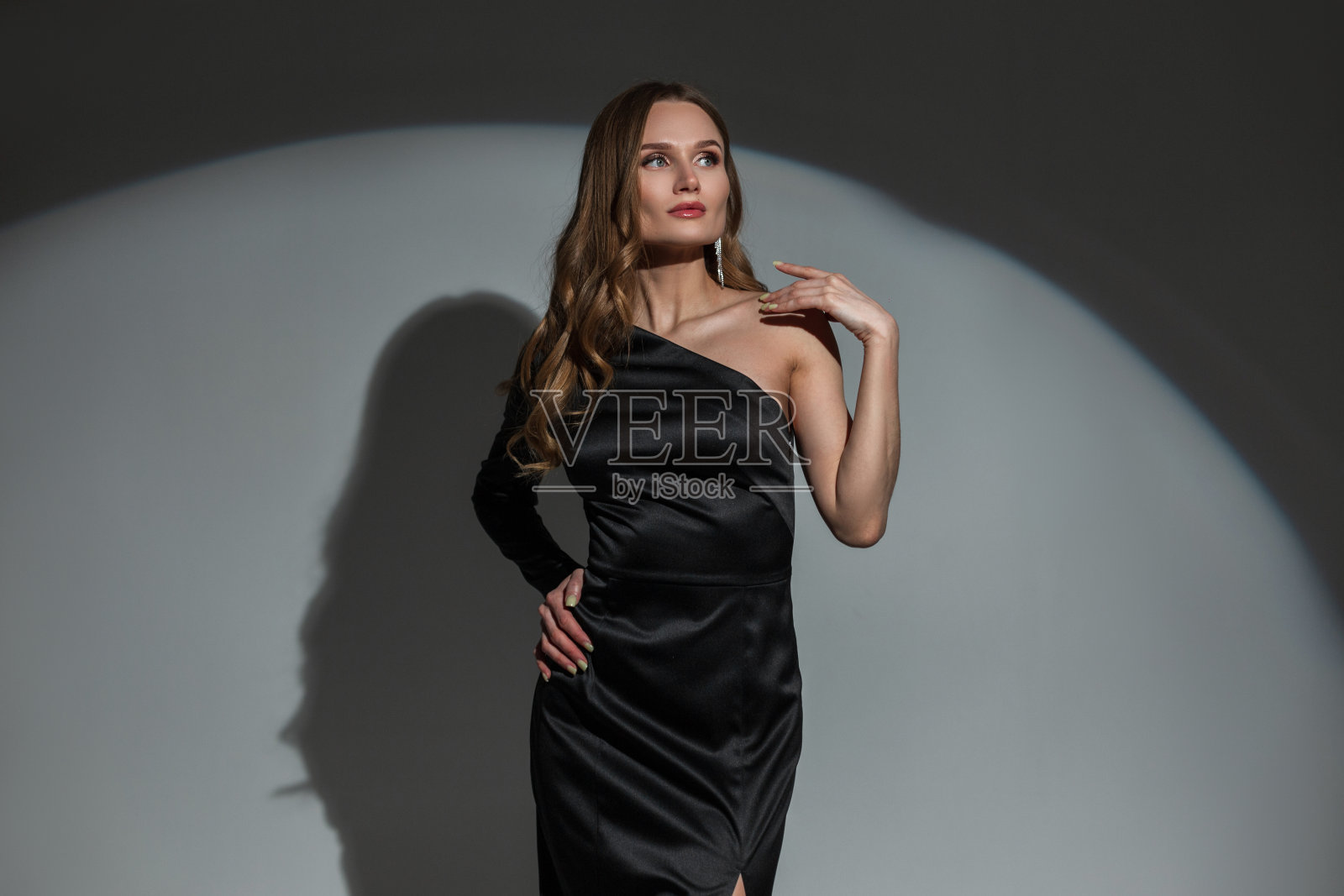 美丽的年轻时尚别致的女人与卷曲的发型，时尚的黑色优雅的礼服在黑暗的背景与圆形光在聚会上。漂亮女士庆祝一件事照片摄影图片