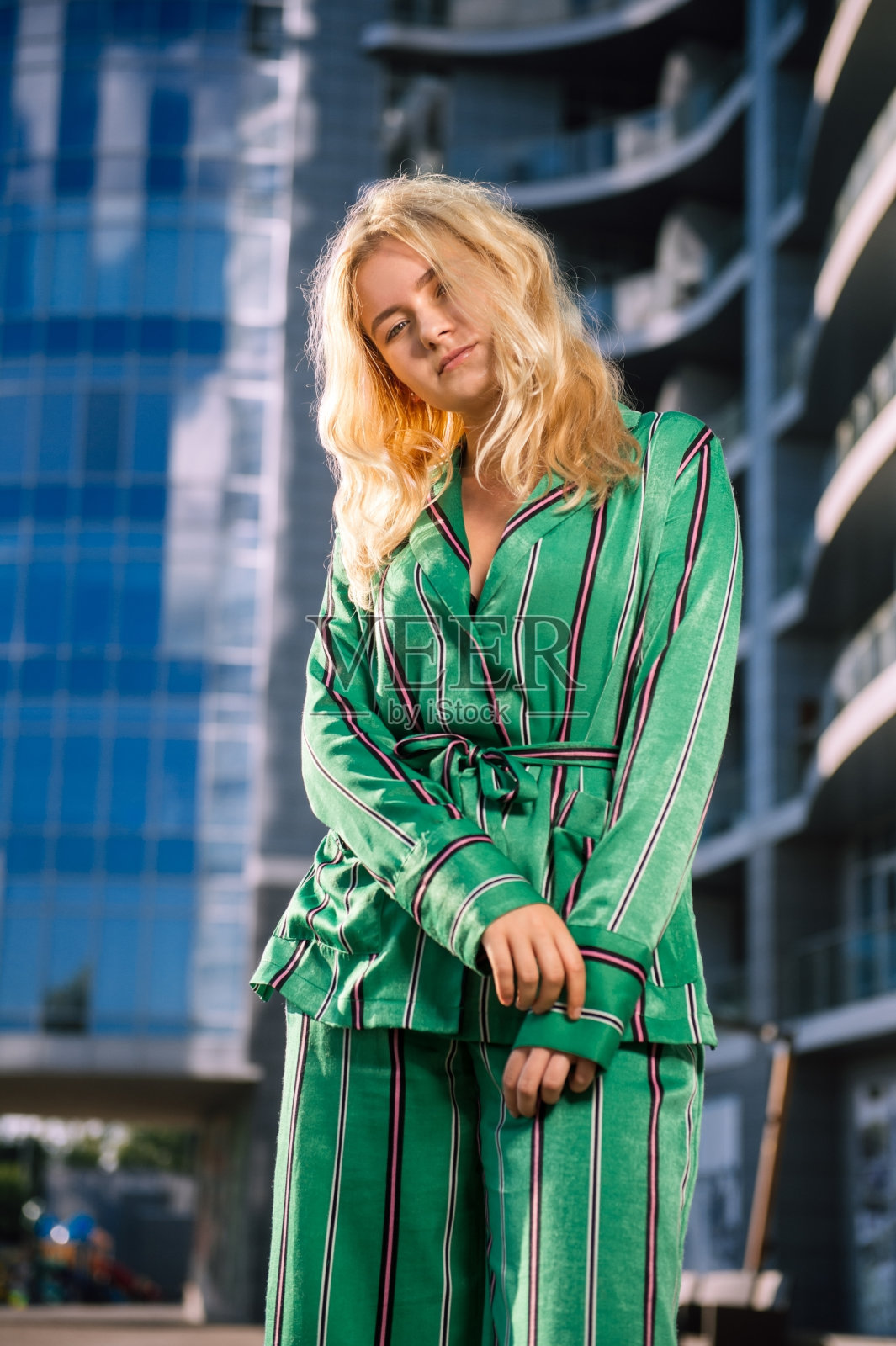 在模糊的城市背景下，穿着绿色套装的漂亮女孩。时髦的金发女郎。时尚的女孩。一个美丽女孩的日常生活。穿着时髦西装的金发美女。阳光下的金发。照片摄影图片