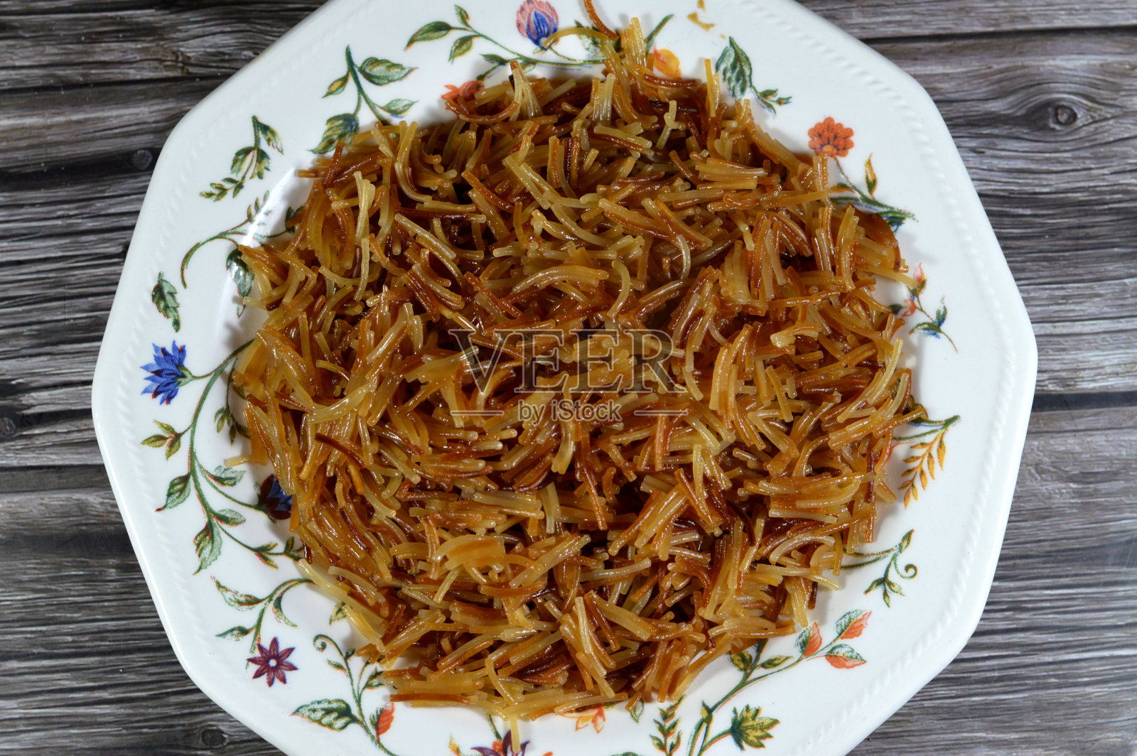 一盘在锅中加水和糖煮熟的棕色埃及甜粉丝。传统的埃及甜点在午餐晚和晚餐早，一个埃及流行的食谱照片摄影图片