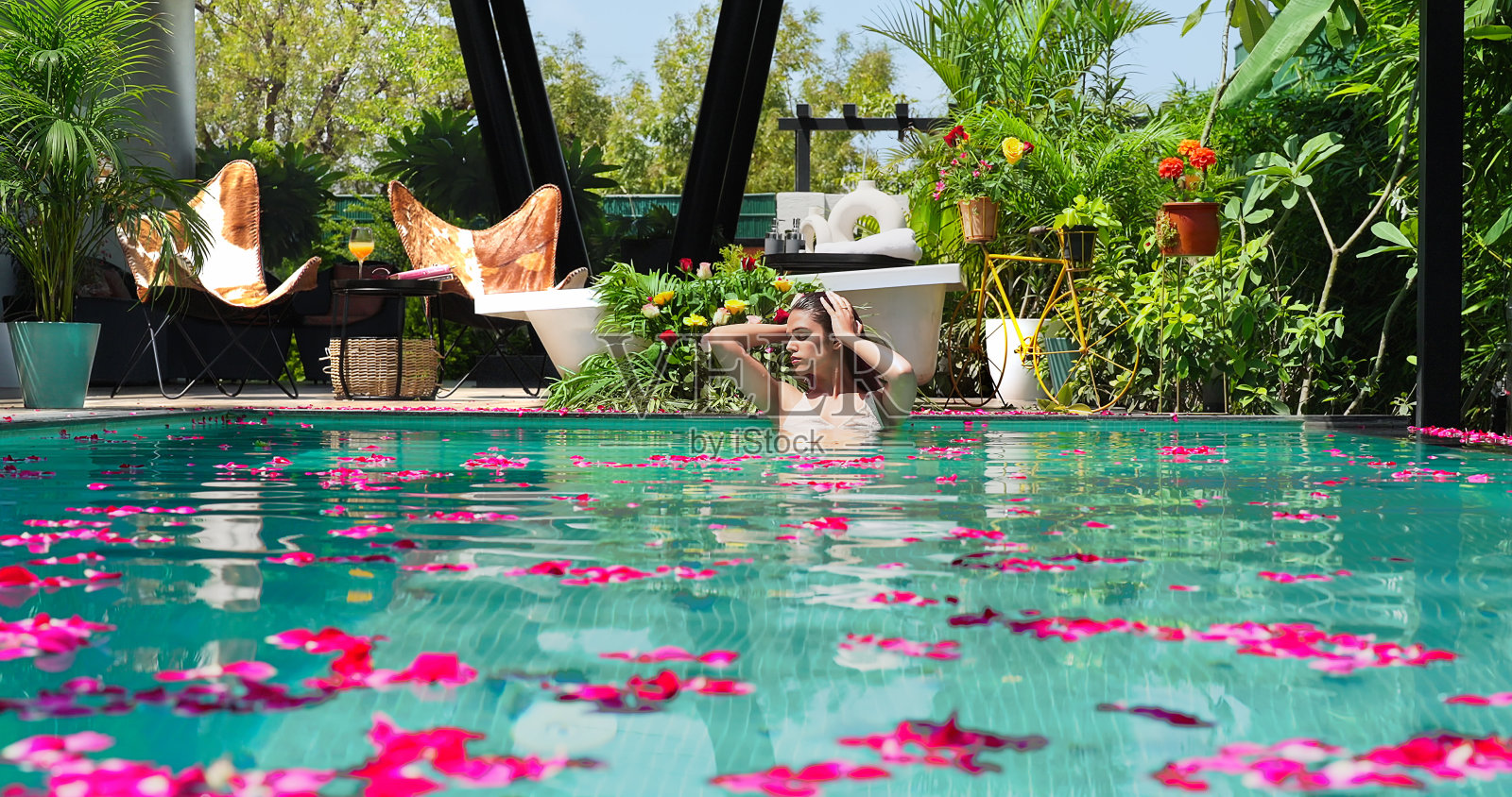 快乐美丽的印度年轻女子放松在游泳池享受暑假户外。微笑的女性在豪华度假胜地早上洗澡，看着镜头在蓝色的水边放松姿势照片摄影图片