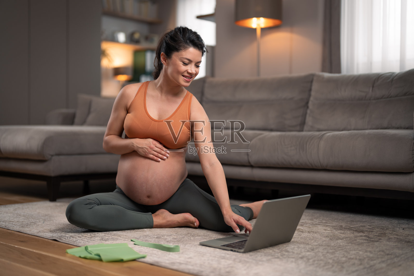 一个快乐的孕妇在她的笔记本电脑上放着锻炼视频，准备在客厅锻炼照片摄影图片