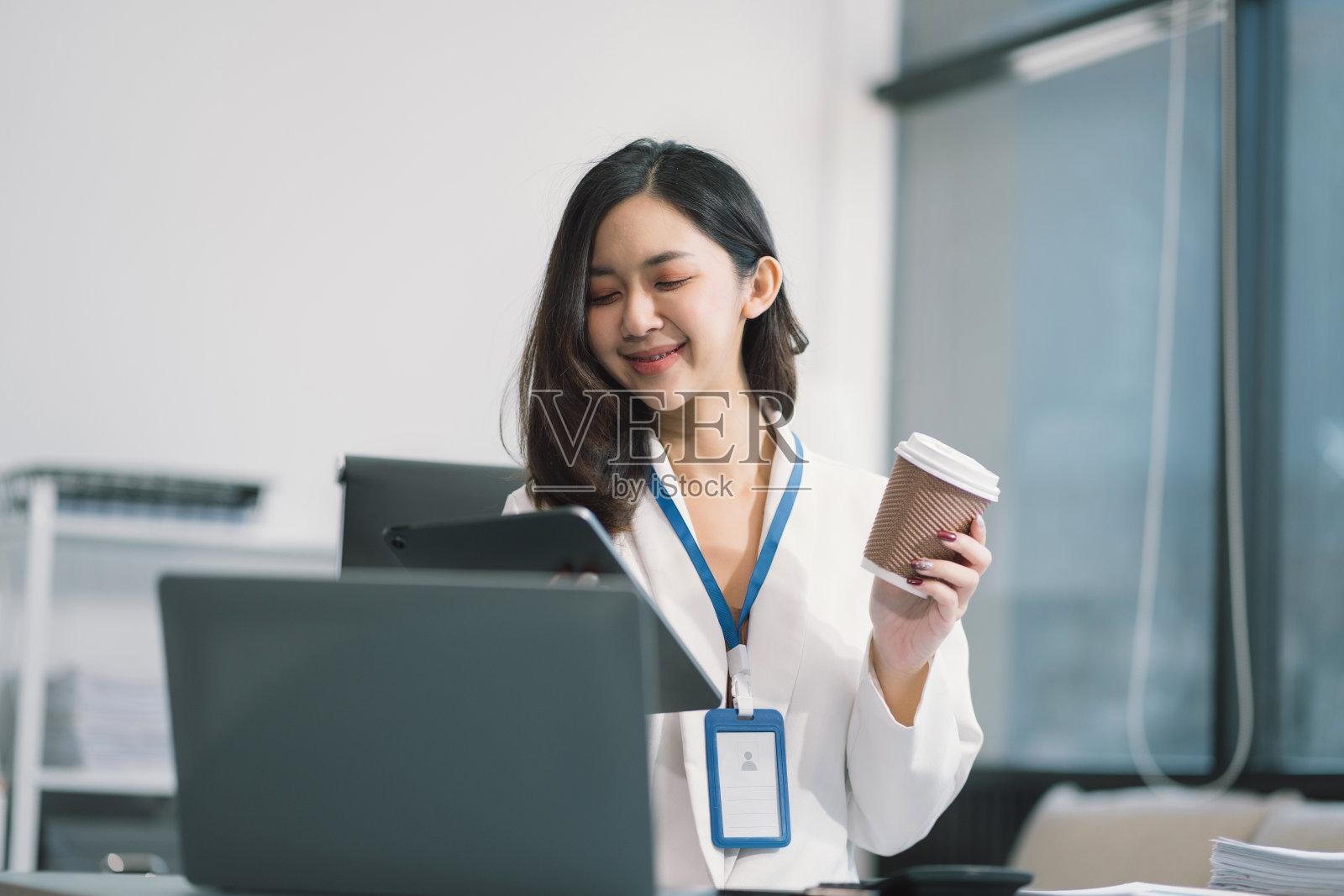 商务女性用笔记本电脑，拿着智能手机，桌上放着咖啡杯。照片摄影图片