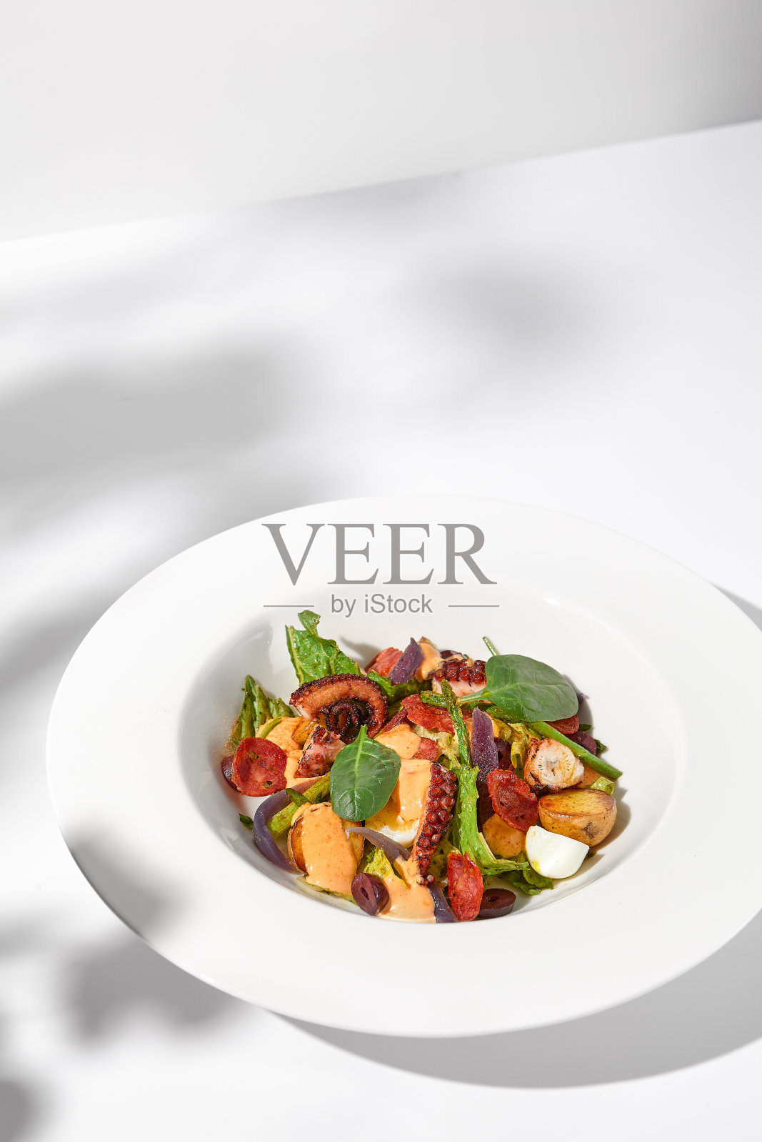 地中海沙拉，用章鱼、土豆、西红柿和卡拉马塔橄榄蘸辣酱，在白色背景上涂上阴影照片摄影图片