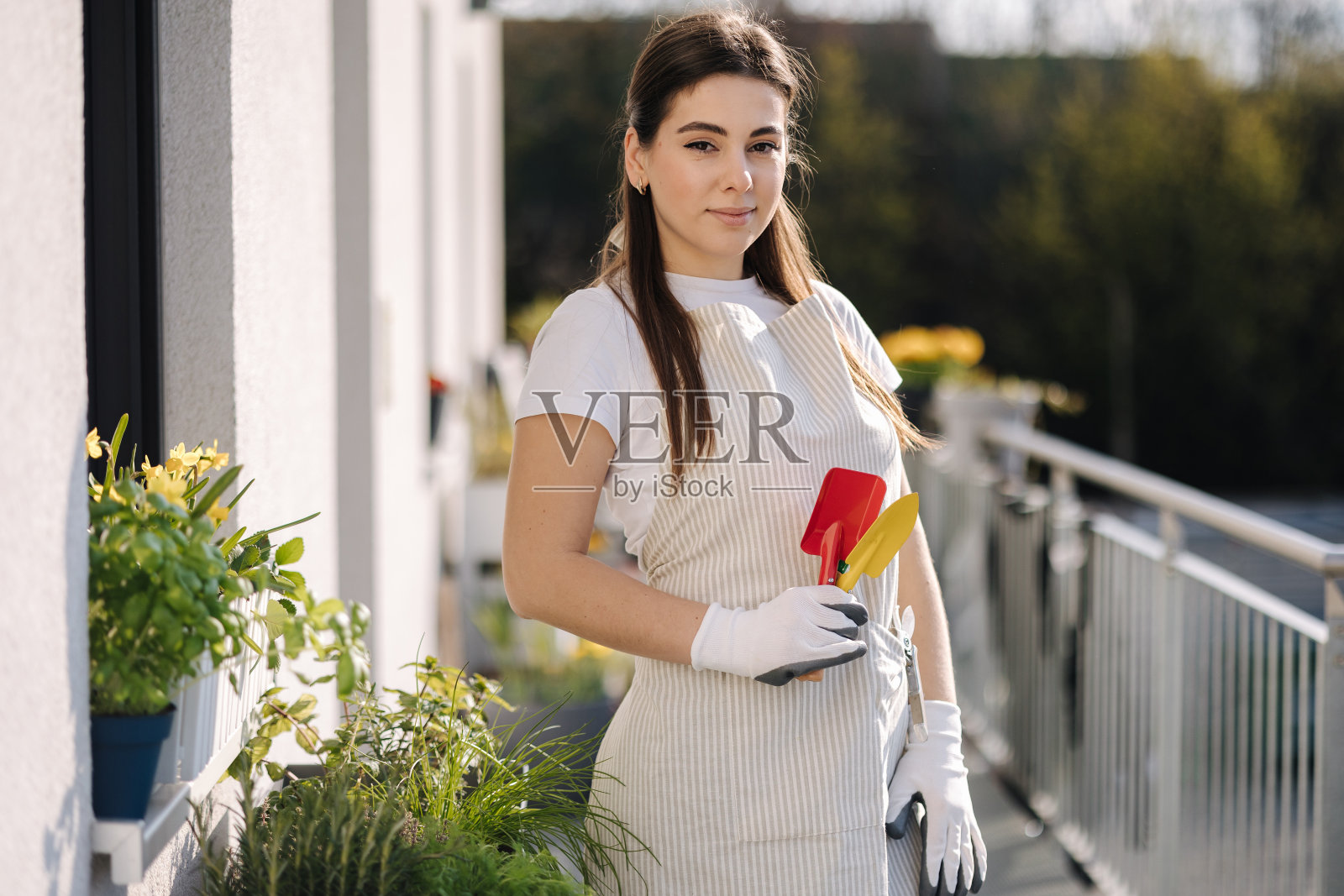 年轻貌美的女性整体手持园林工具站在阳台上准备落地照片摄影图片