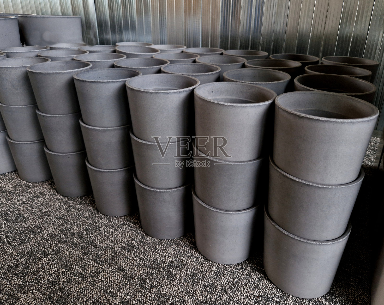 灰色的混凝土花盆，在仓库里排成一排待售。白色的塑料砖堆在一起。生产廉价设计的植物容器、地毯照片摄影图片