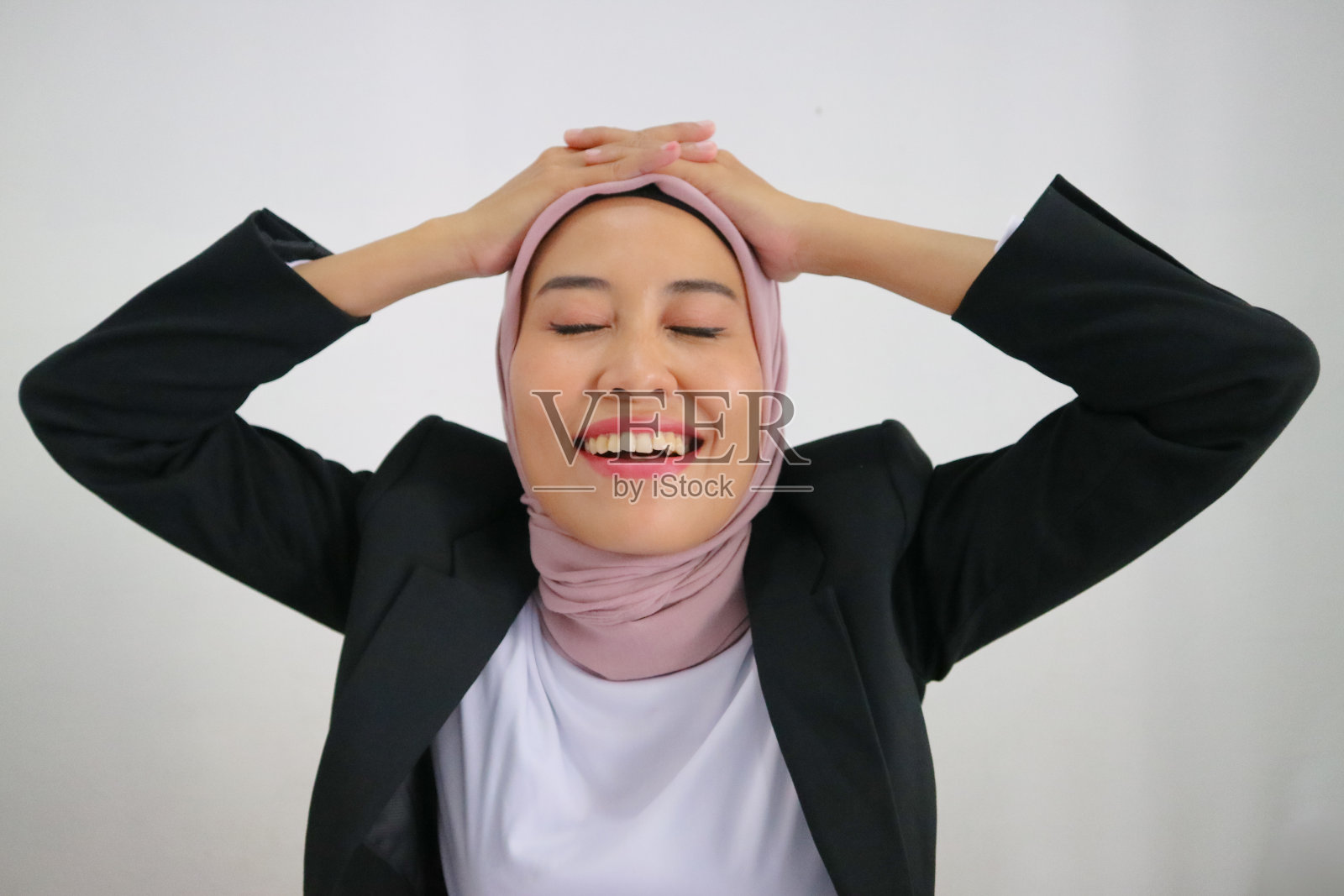 肖像一个快乐的梦幻美丽的亚洲妇女享受闭着眼睛和有趣的可爱的微笑在白色的背景上穿着正装。手放在头上。照片摄影图片