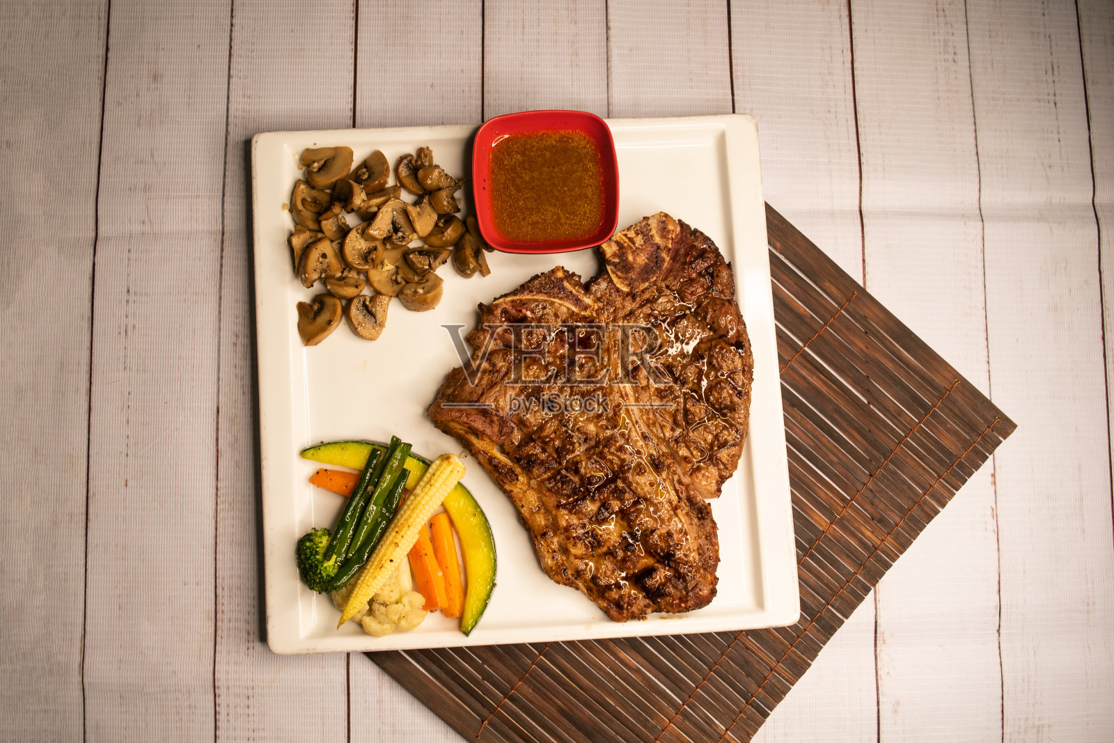 T骨牛排，烤肉配酱汁，蘑菇和沙拉，放在餐巾纸上的盘子里，木质餐桌上的意大利菜照片摄影图片