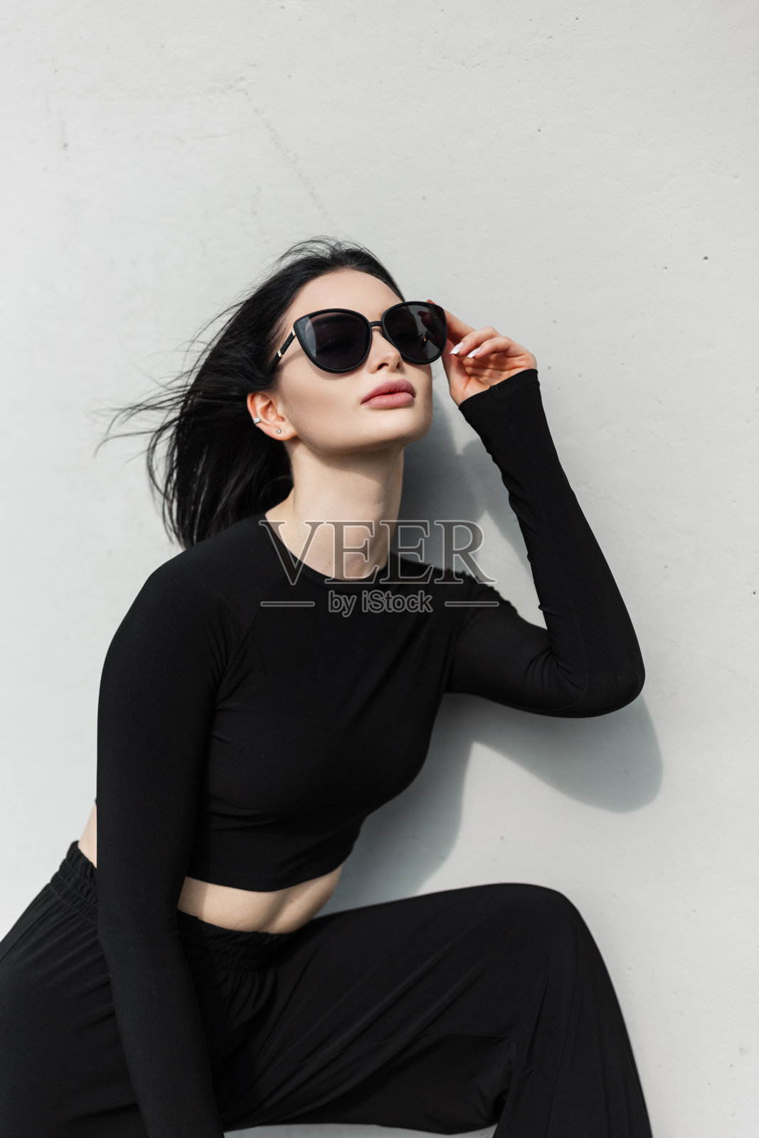 酷酷的时尚都市时髦美女，穿着时尚的黑色运动服，戴着时尚的黑色太阳镜，在街上的灰色墙壁旁摆姿势照片摄影图片