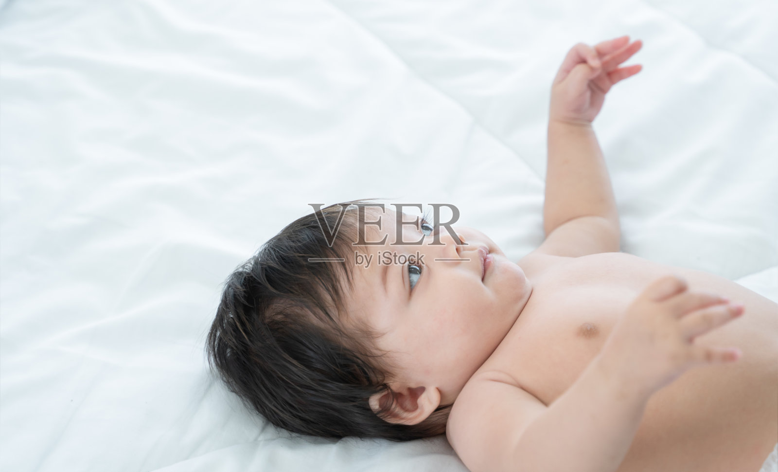 3个月大的婴儿躺在白色的床和毯子上。可爱的混血儿，亚洲白种人，婴儿躺在床上，微笑。家里卧室里穿着尿布的小女孩照片摄影图片