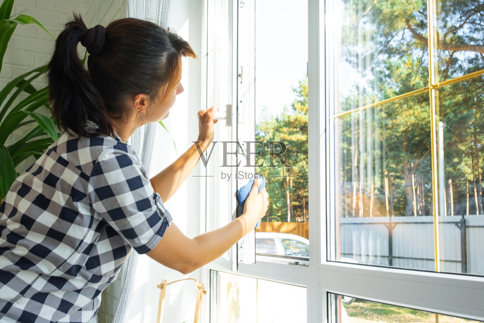 妇女用带有喷雾清洁剂的抹布和拖把手动清洗房子的窗户，室内有白色窗帘。恢复春天的秩序和清洁，清洁服务照片摄影图片