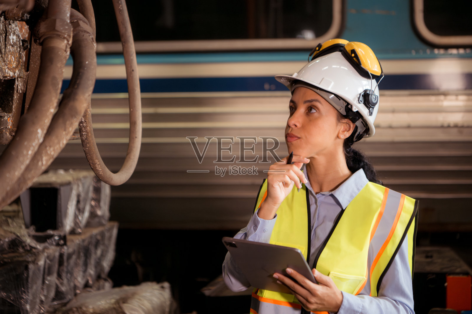 穿着安全背心和头盔的铁路技术工人在火车维修站拿着写字板工作的肖像照片摄影图片