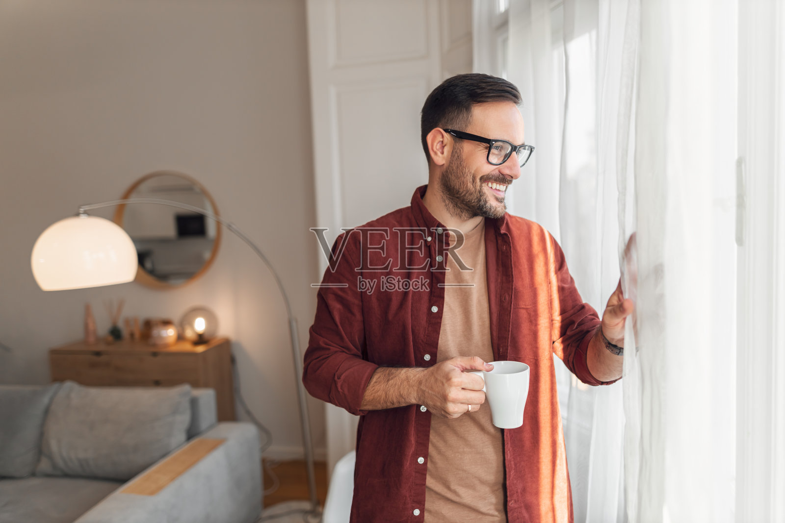 一个满意的远程工作的成年男性在家里喝着一杯咖啡，看着窗外照片摄影图片