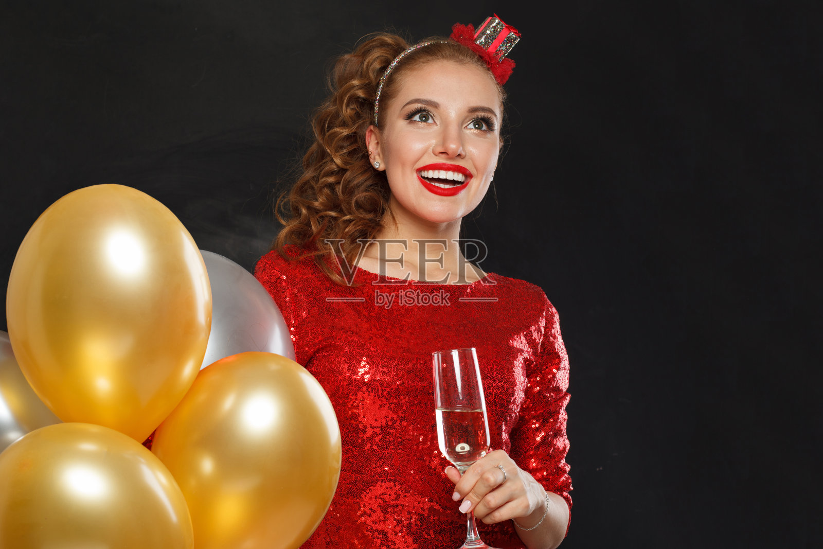 美丽的快乐惊喜的女人化妆和发型穿着红色闪亮的亮片礼服拿着派对气球，惊喜，礼物和圣诞假期庆祝背景照片摄影图片