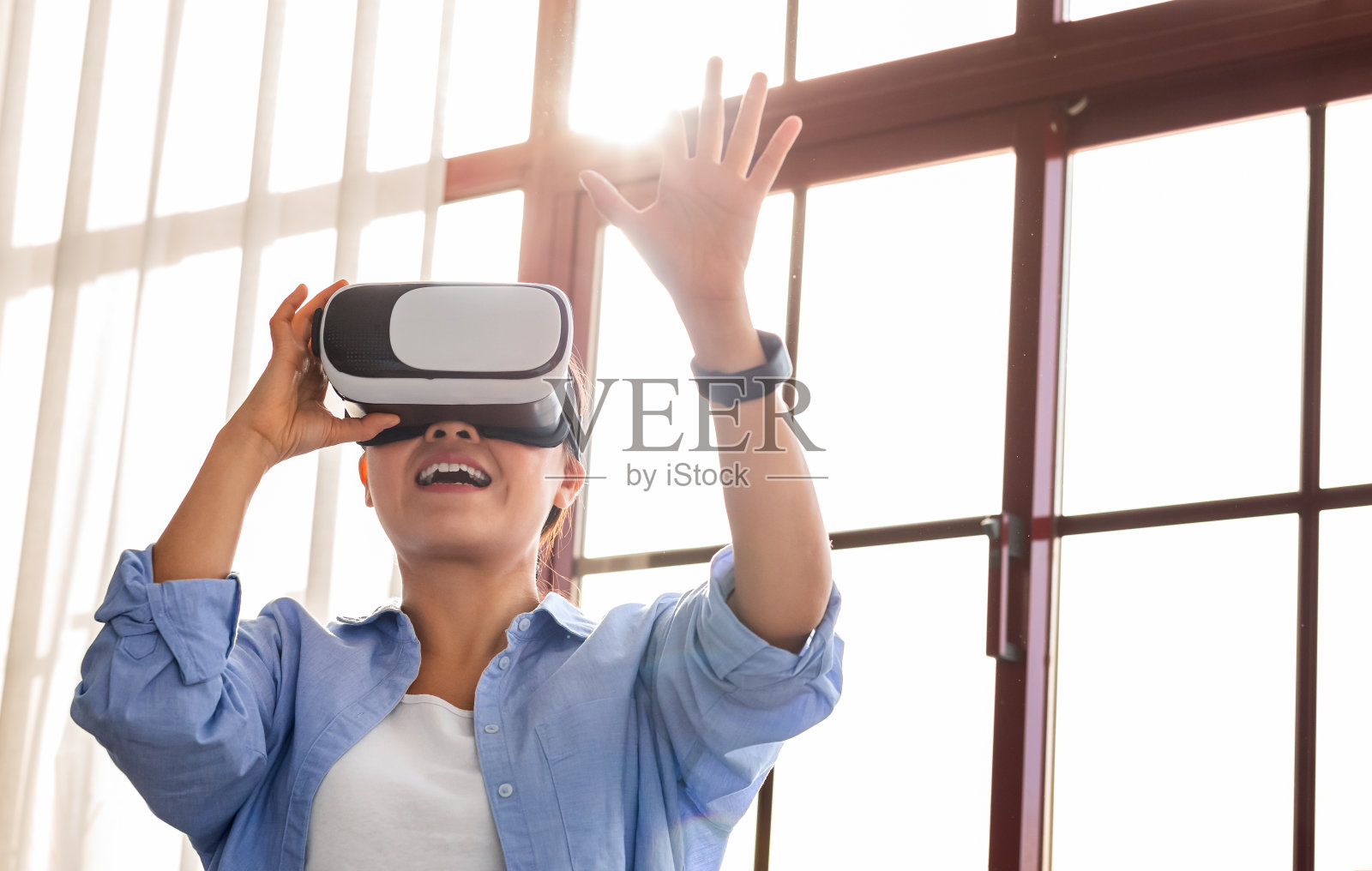 快乐的年轻亚洲女人戴着虚拟现实耳机站在窗边照片摄影图片