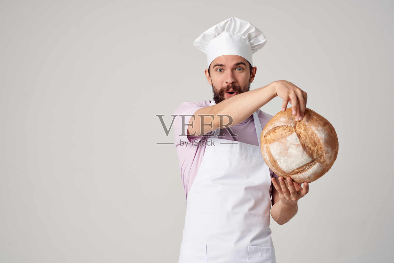 系着白围裙的男面包师，手里拿着专业人士的面包照片摄影图片