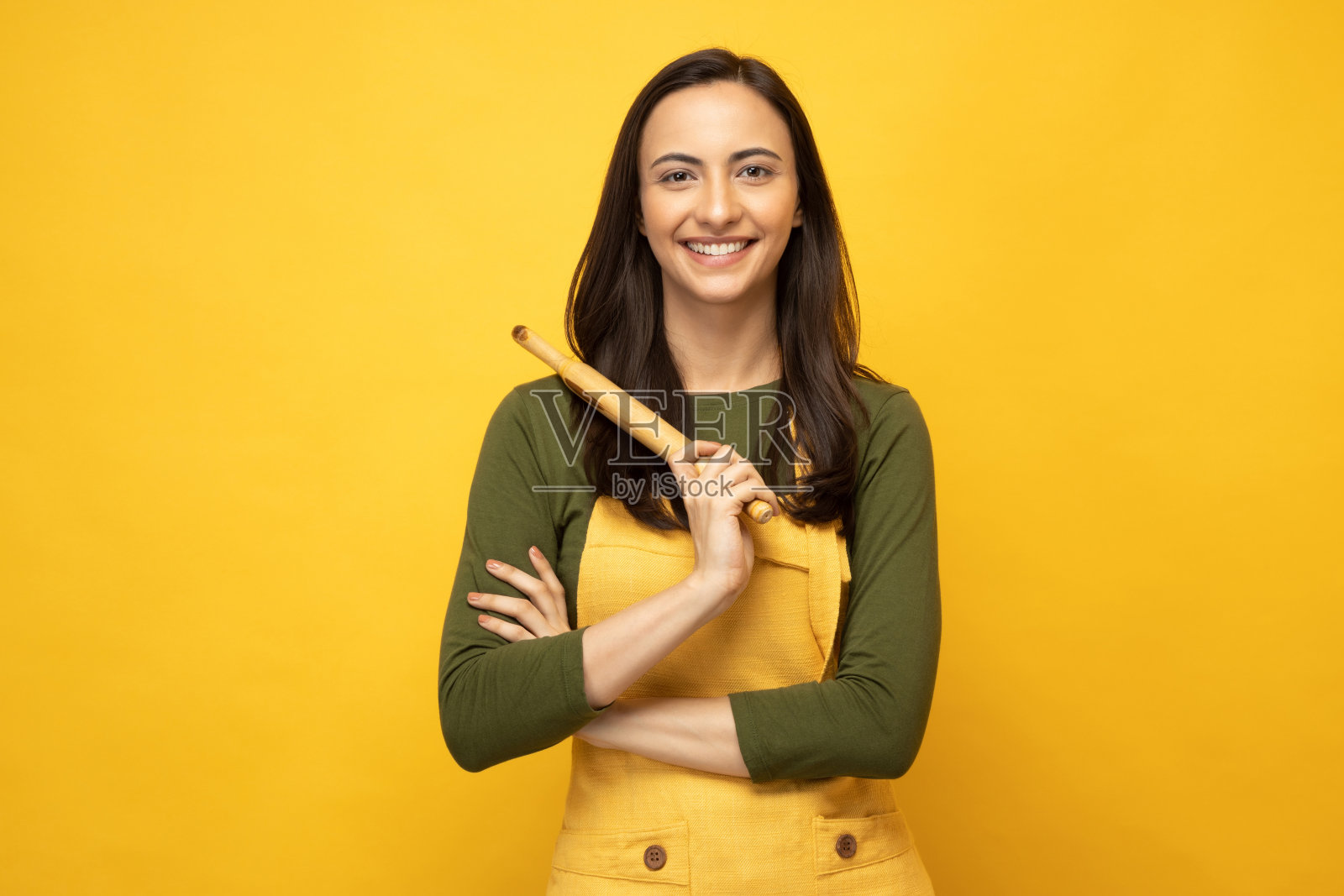 印度女厨师戴着围裙，拿着木制擀面杖，孤立地站在黄色背景照片上照片摄影图片