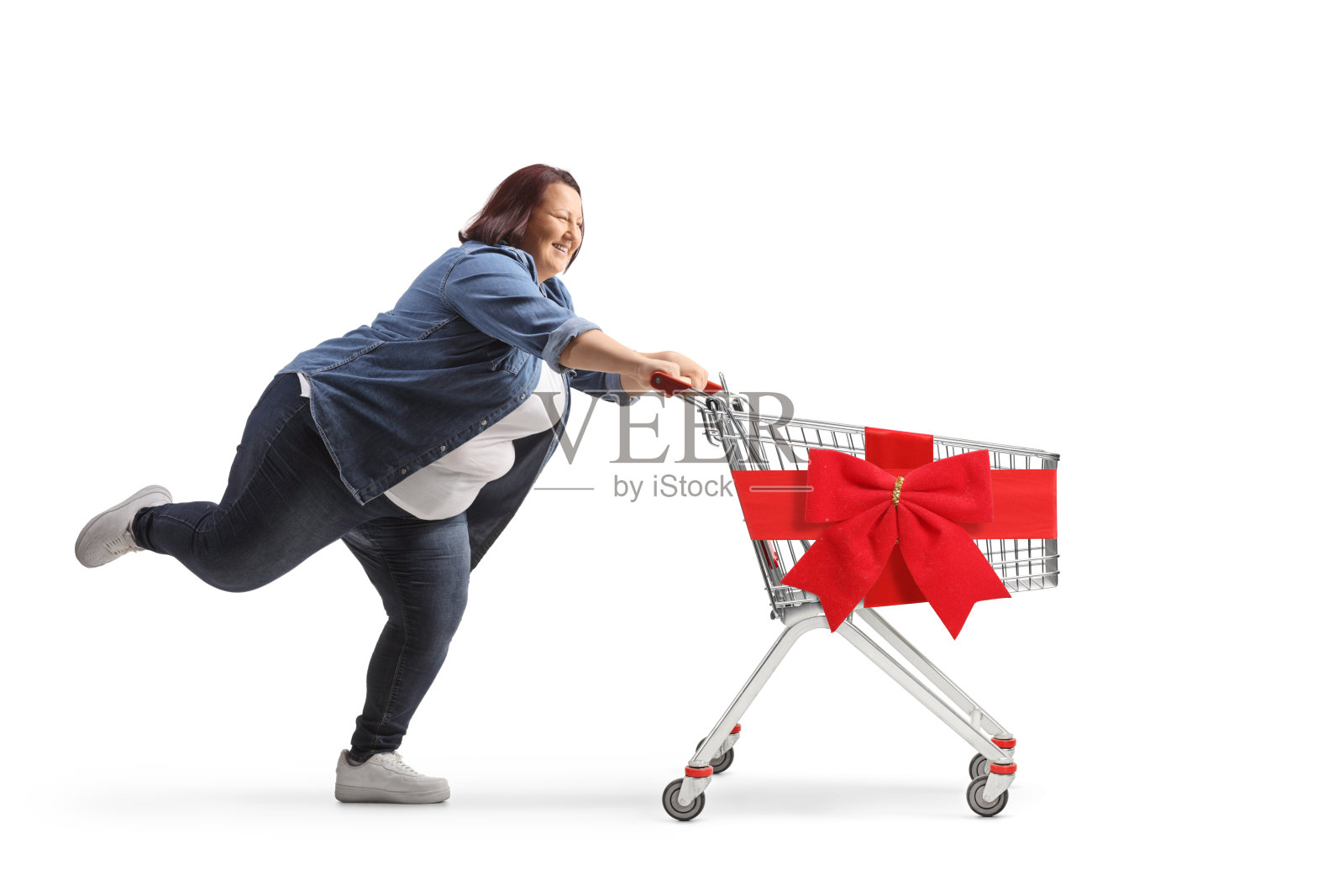 一个肥胖的女人带着红丝带蝴蝶结拎着空荡荡的购物车跑着照片摄影图片