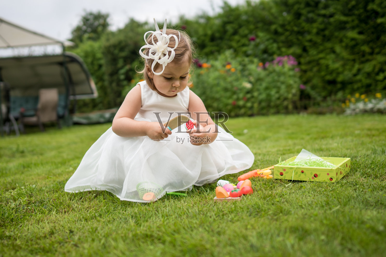 可爱的小女孩穿着白色的裙子坐在绿色的草地上玩玩具照片摄影图片