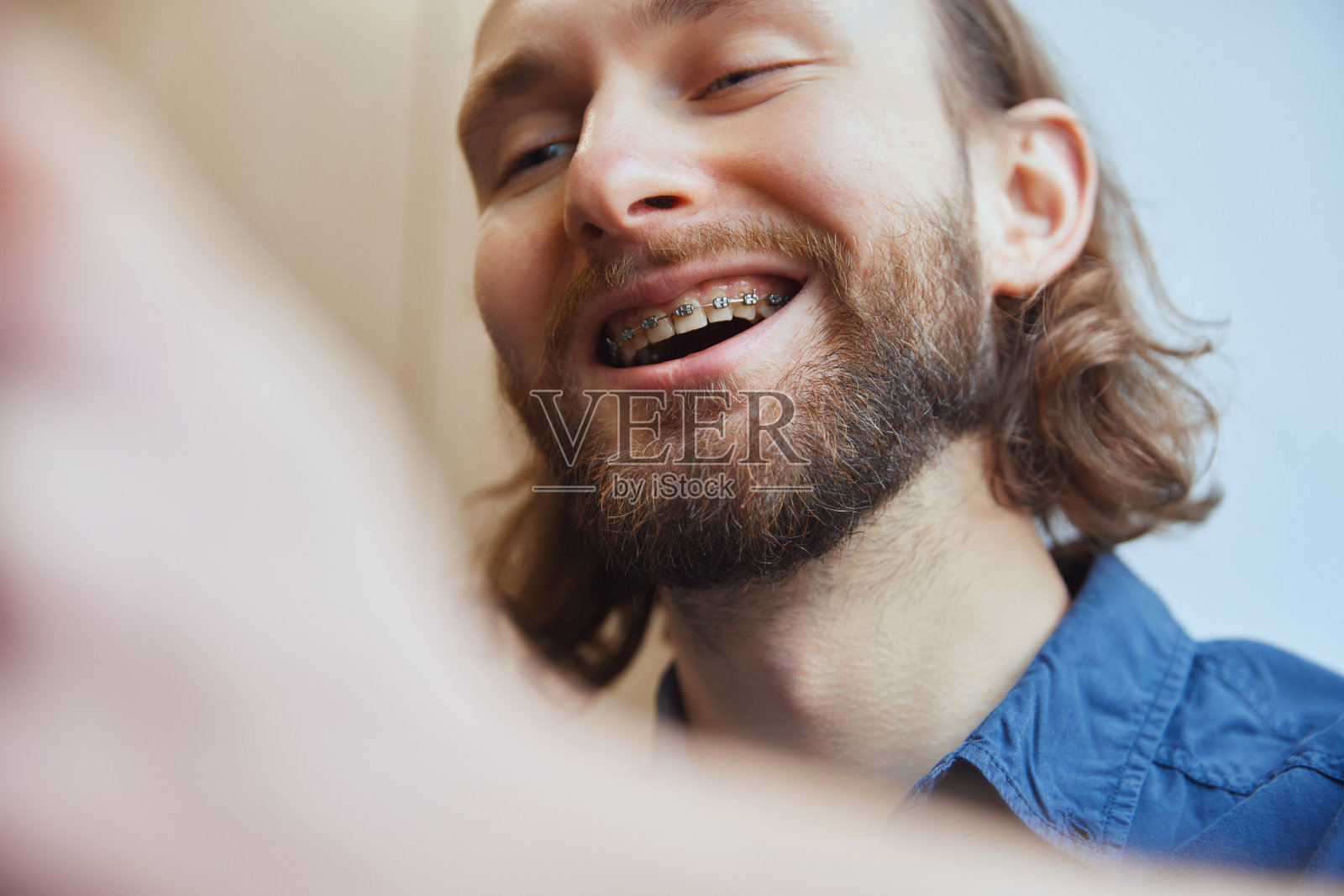 一个戴着牙套微笑的快乐男人坐在厨房里看手机的特写。有选择性的重点。照片摄影图片