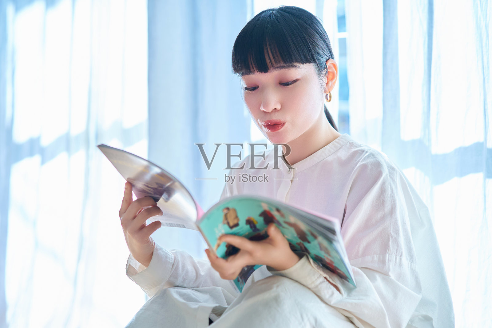 在窗边看杂志的年轻女子照片摄影图片