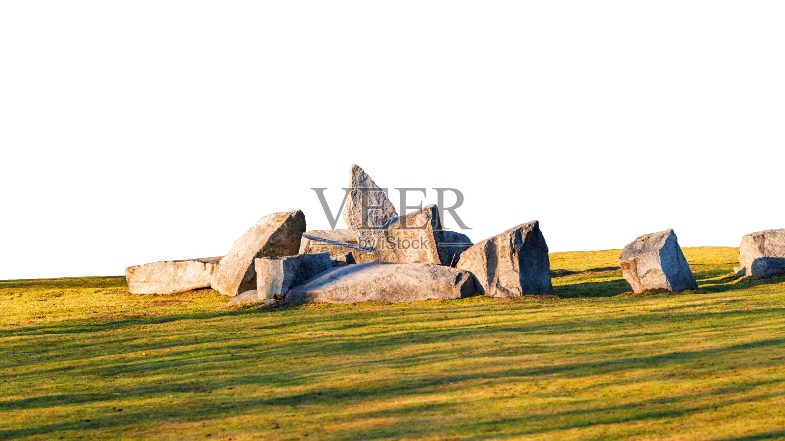 在夕阳照射下的草坪上，巨石的构图与背景分开，形成长长的阴影。照片摄影图片