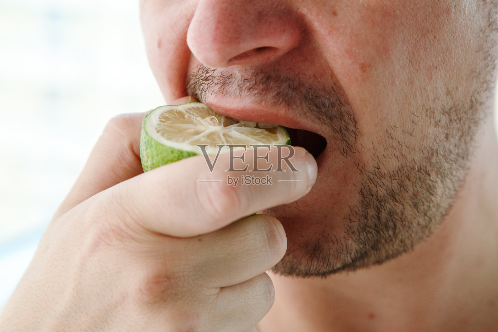 一个男人的嘴吃着酸橙，新鲜的果汁充满了维生素照片摄影图片