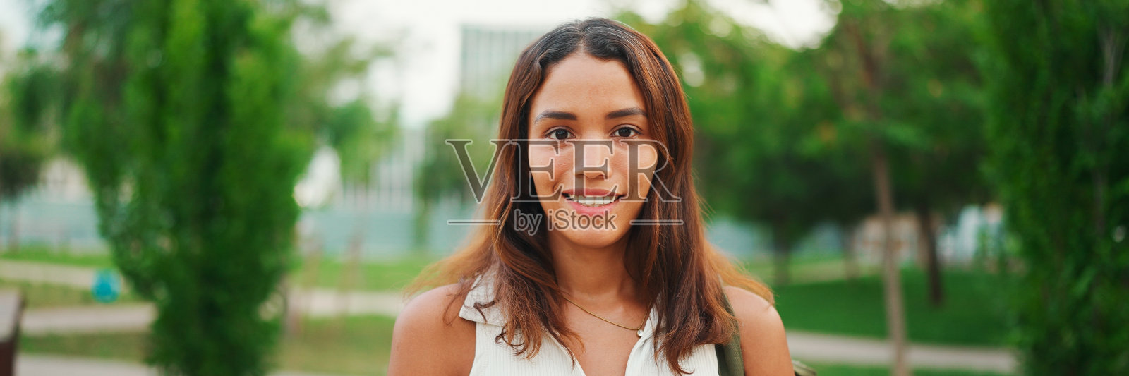 一头棕色长发，皮肤黝黑，穿着白色上衣的美丽女孩抬起头，直视镜头，全景照片摄影图片