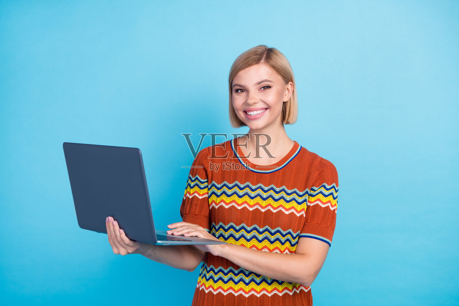 肖像的牙齿笑容女孩与短发型穿着条纹t恤持有笔记本电脑打字电子邮件孤立的蓝色背景照片摄影图片