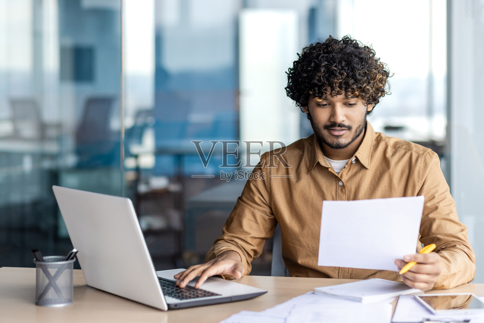 一位留着卷发的年轻商人坐在办公室里，沉浸在他的笔记本电脑前，制作着一件数码杰作照片摄影图片