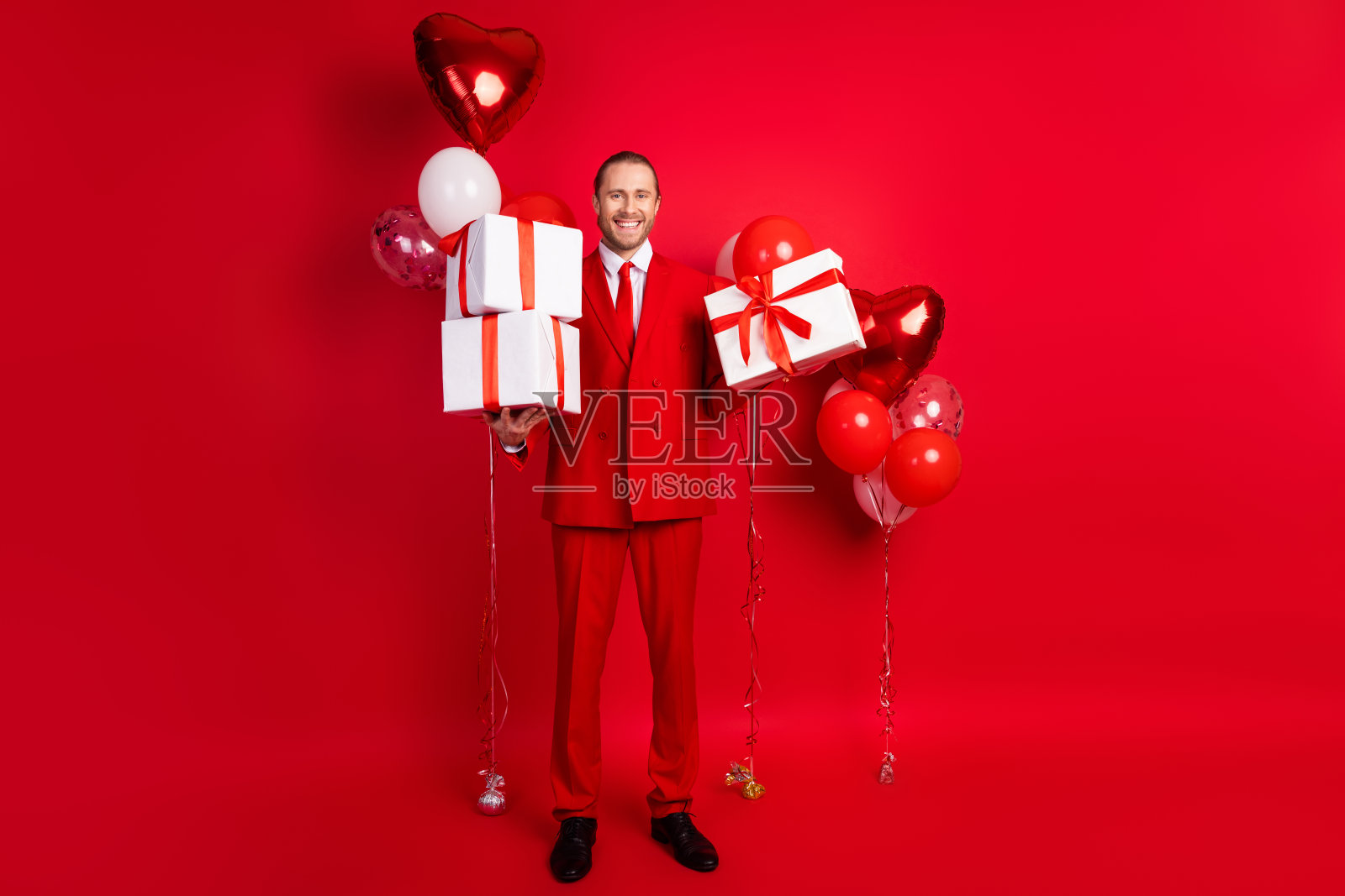 有魅力的年轻人的全身照片拿着礼物气球穿着时髦的经典服装孤立在红色背景照片摄影图片