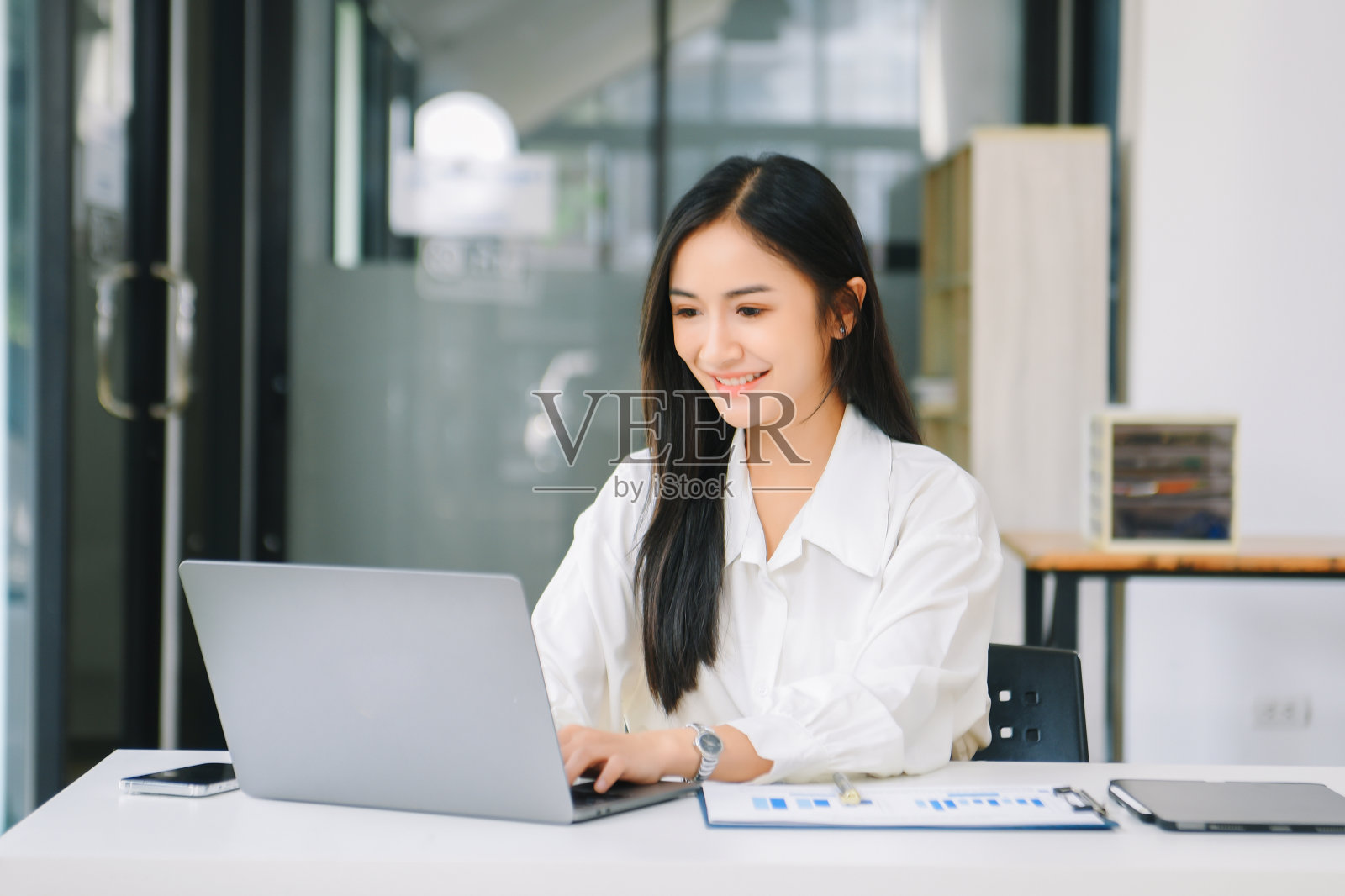 年轻的亚洲女商人用记事本、平板电脑和笔记本电脑工作，在智能手机、平板电脑和笔记本电脑上进行视频通话照片摄影图片