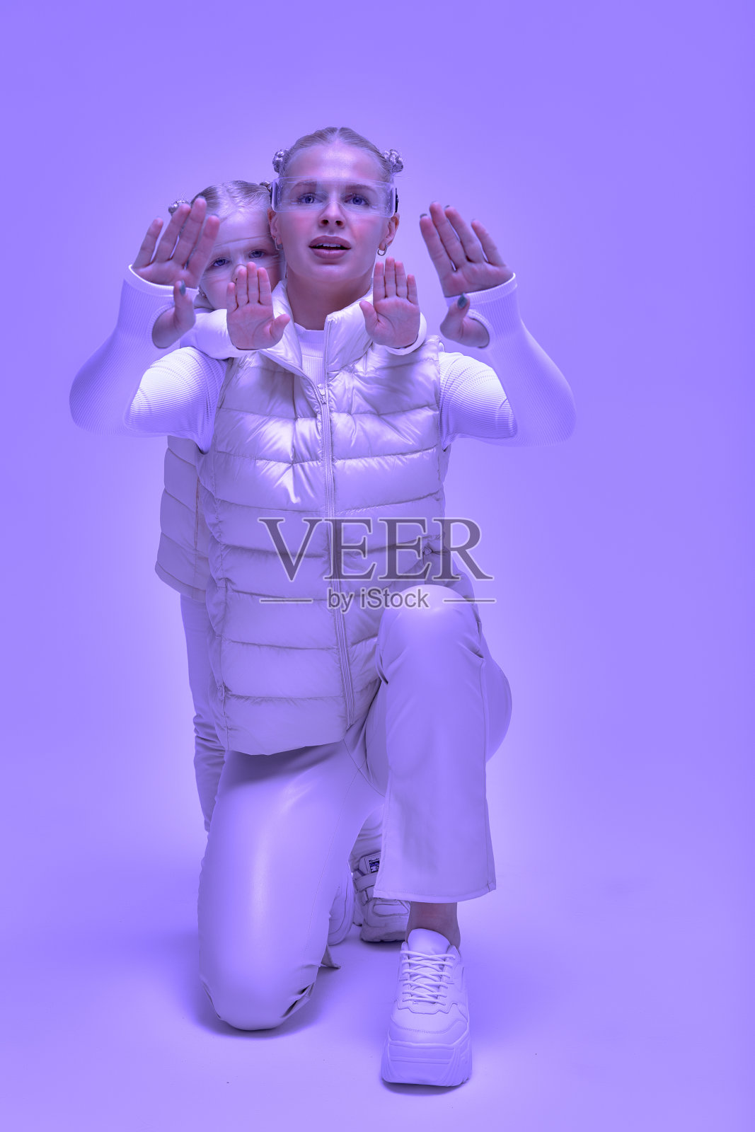 穿着未来主义服装的女人带着小女孩，戴着智能led虚拟现实眼镜，触摸空气。增强现实游戏，未来技术，AI概念。虚拟现实。霓虹灯。照片摄影图片