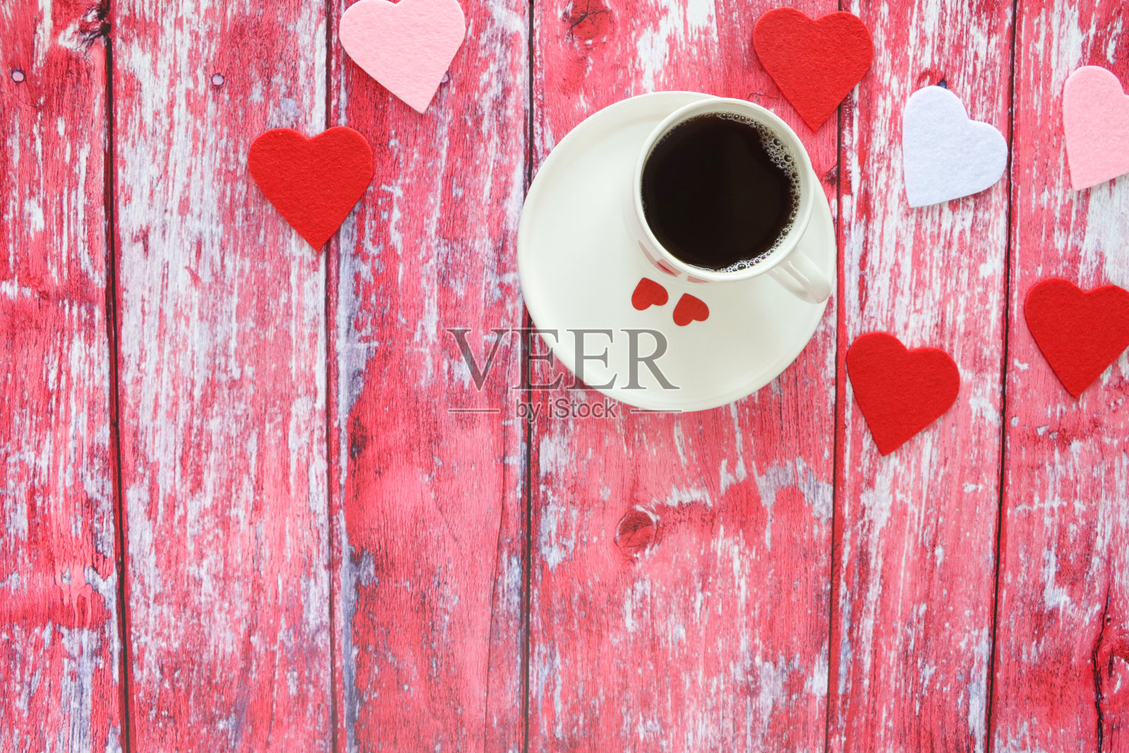白色瓷杯和茶托的特写图像，满是黑色浓缩咖啡，周围是红色，粉红色和白色的心形，粉红色木纹背景，抬高的视图，情人节和浪漫的概念照片摄影图片