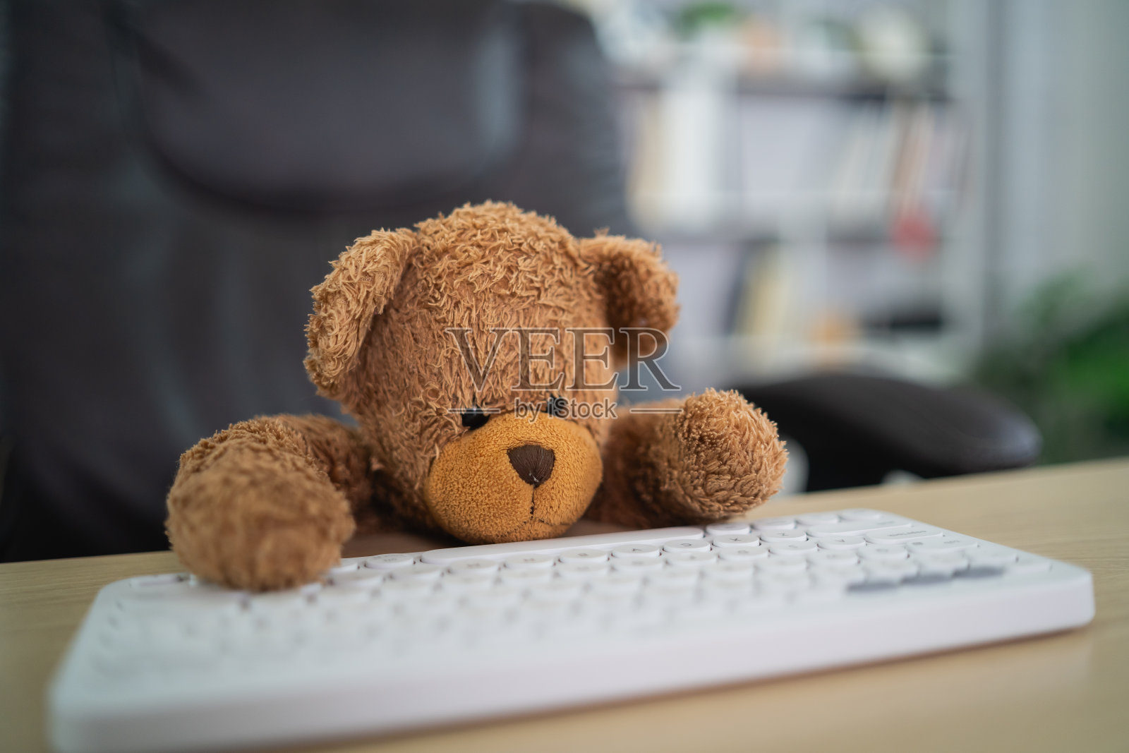 棕色的泰迪熊坐在桌子上躺在白色的键盘上看起来很累。抑郁是悲伤的概念。照片摄影图片