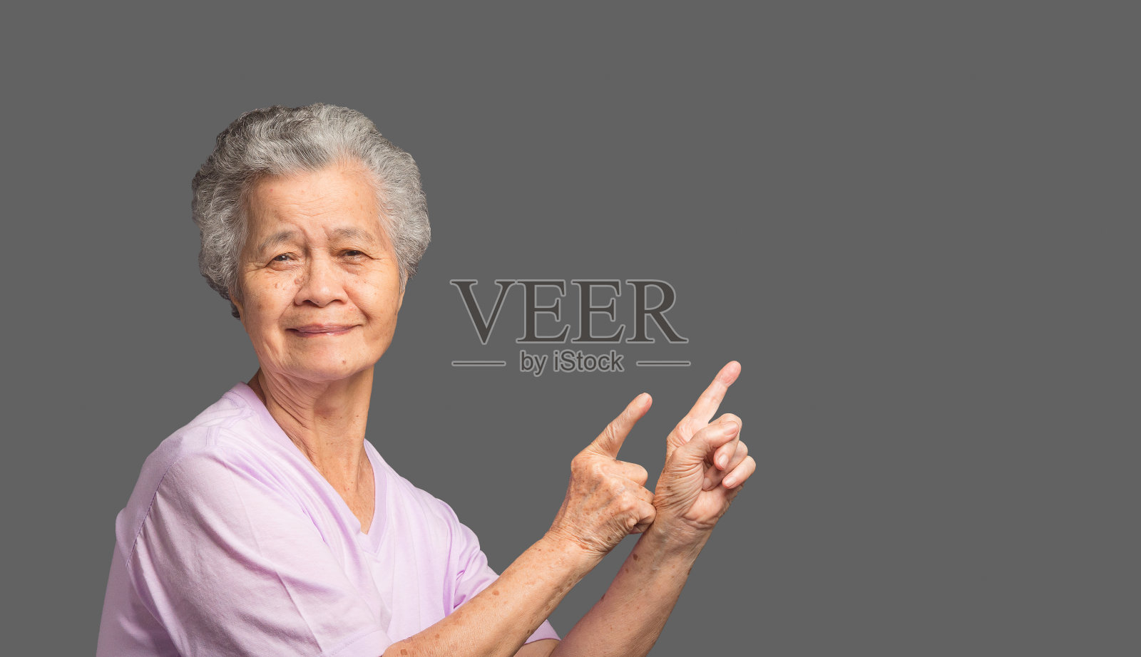 一位年长的亚洲妇女站在黑色背景上，用两只手和手指指着旁边照片摄影图片