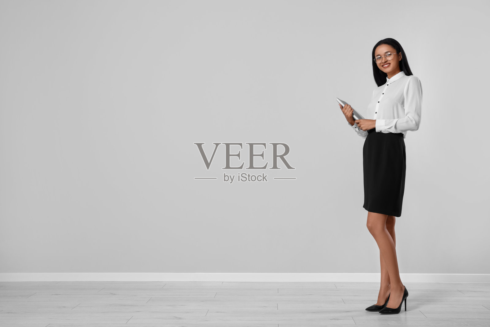 漂亮的秘书拿着文件夹靠近办公室浅灰色的墙壁，留出文字的空间照片摄影图片