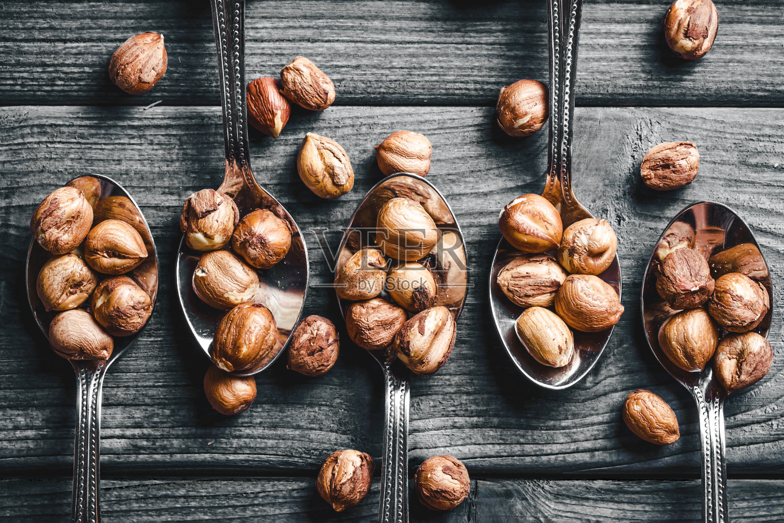 榛子的背景。把坚果放在勺子上。五把银勺子放在灰色的木头上。木桌坚果背景。照片摄影图片
