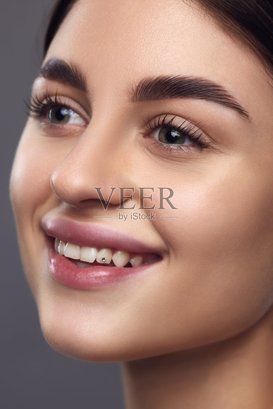 特写女模特的脸，完美的嘴唇和眼妆微笑着看着灰色的工作室背景。照片摄影图片