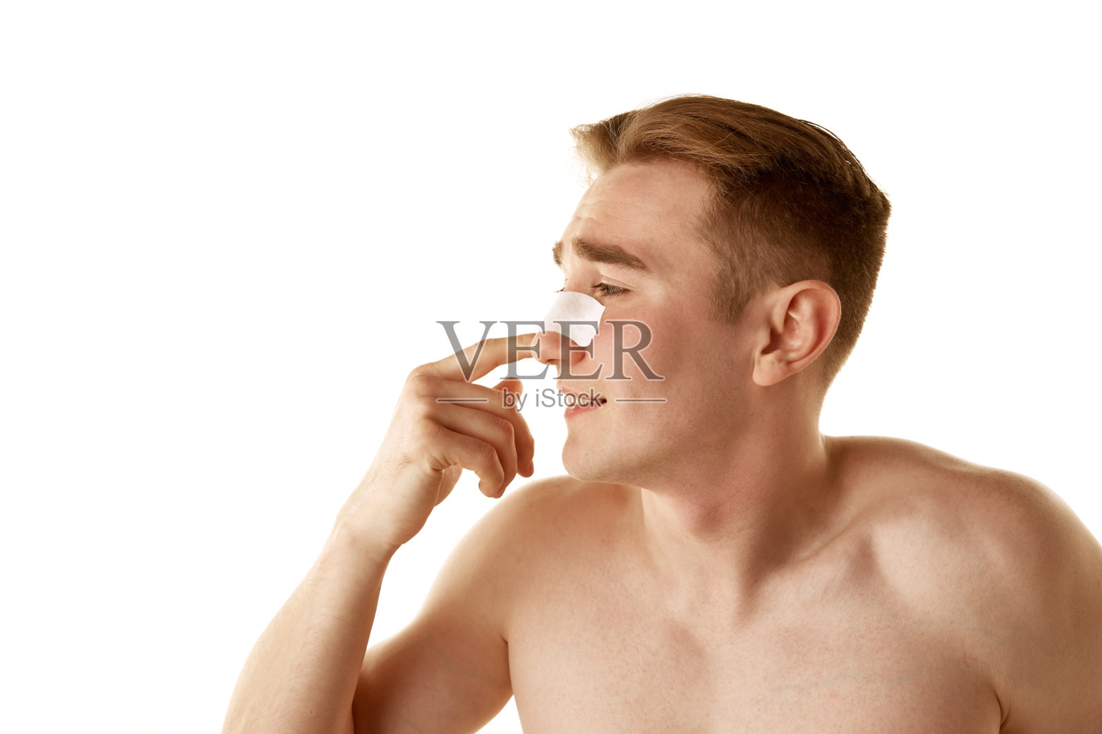 年轻赤膊男士洗脸后，在鼻子上涂抹清洁毛孔、去黑头贴片，隔离在白底上照片摄影图片