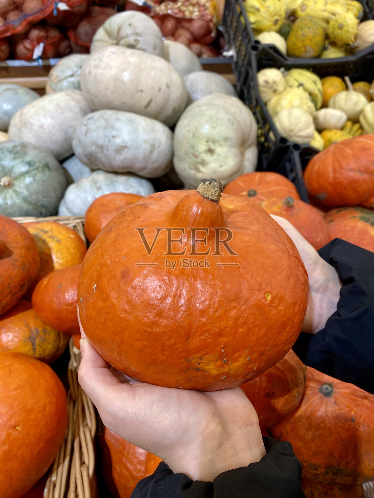 一名男子手里拿着熟透的南瓜，在商店里挑选蔬菜。照片摄影图片