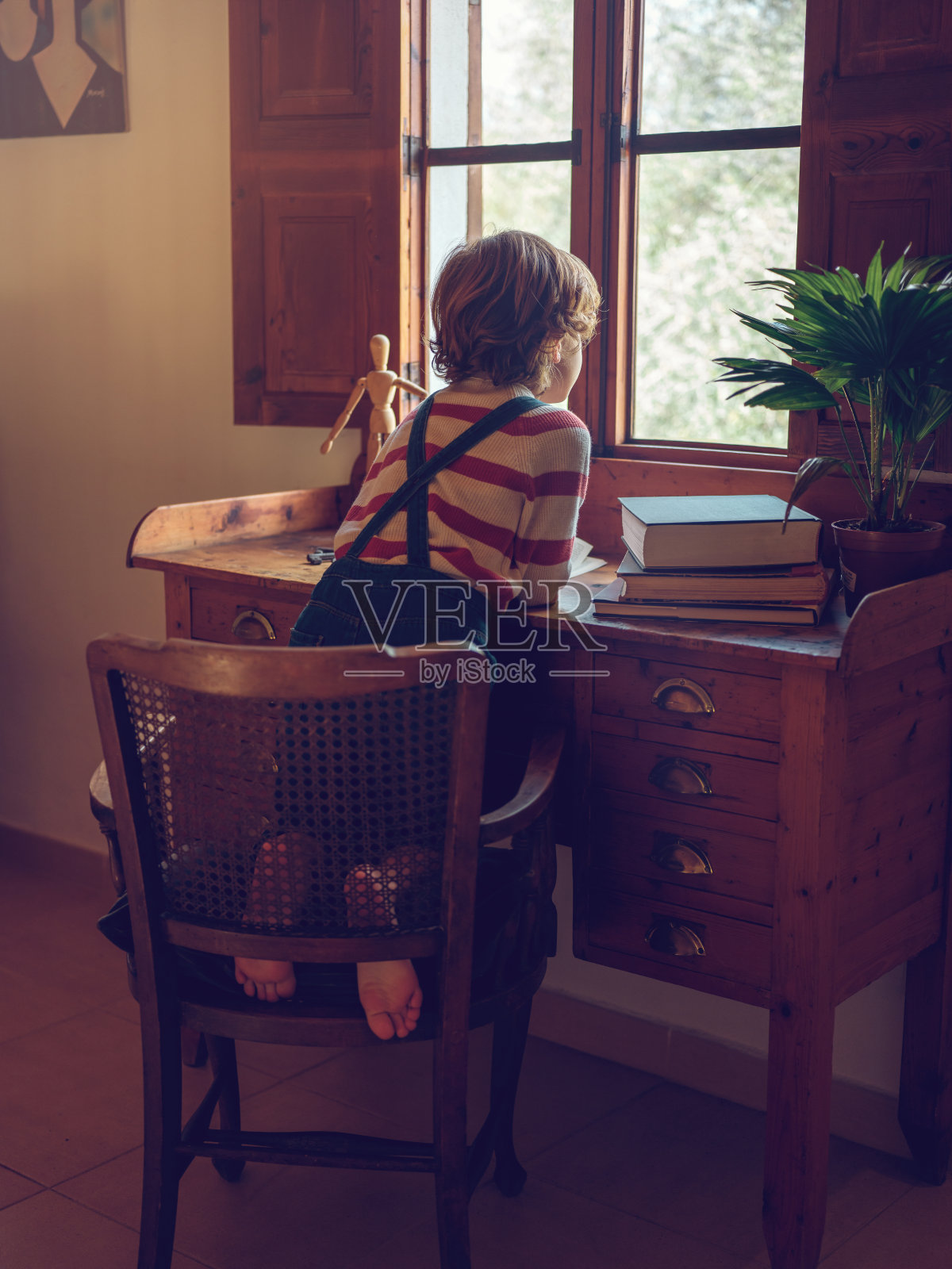 面目全非的孩子靠在桌子上，望着窗外照片摄影图片