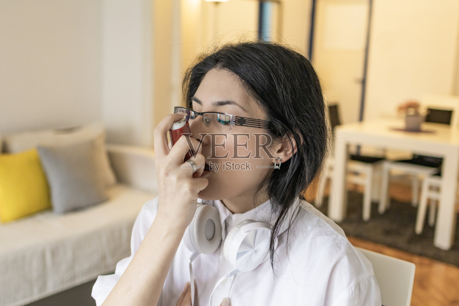 一名妇女在哮喘病发作时正在使用哮喘病泵，吸入器，同时在她的家庭办公室工作。情绪和身体上的压力。现代虚拟理财顾问和咨询。远程办公，商务，自由职业者，网上购物，电子学习。照片摄影图片